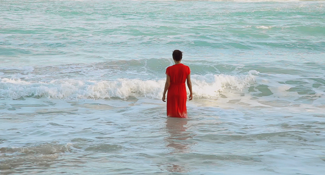 haitian woman in red dress standing in ocean waves