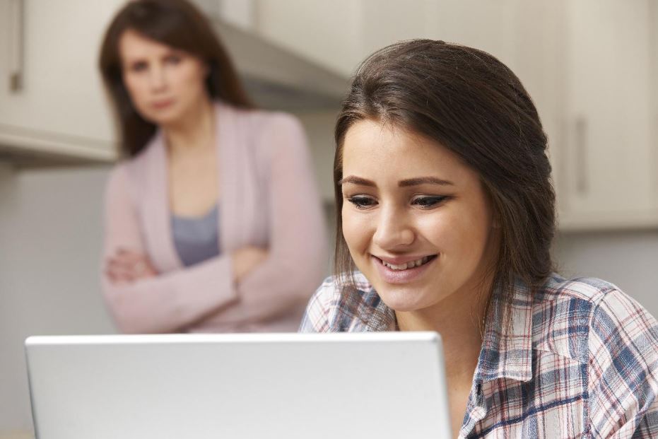 teen girl on laptop computer with mom in the background