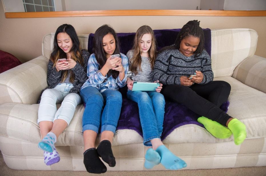 teen girls sitting on sofa using tech