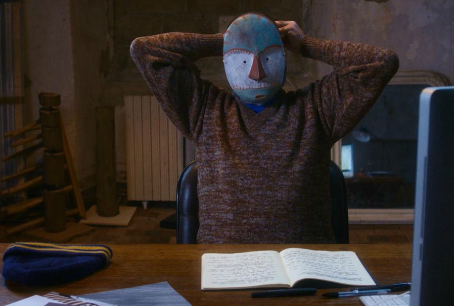 man sitting at desk wearing tribal mask