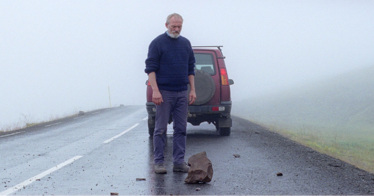 man looking at rock in the road