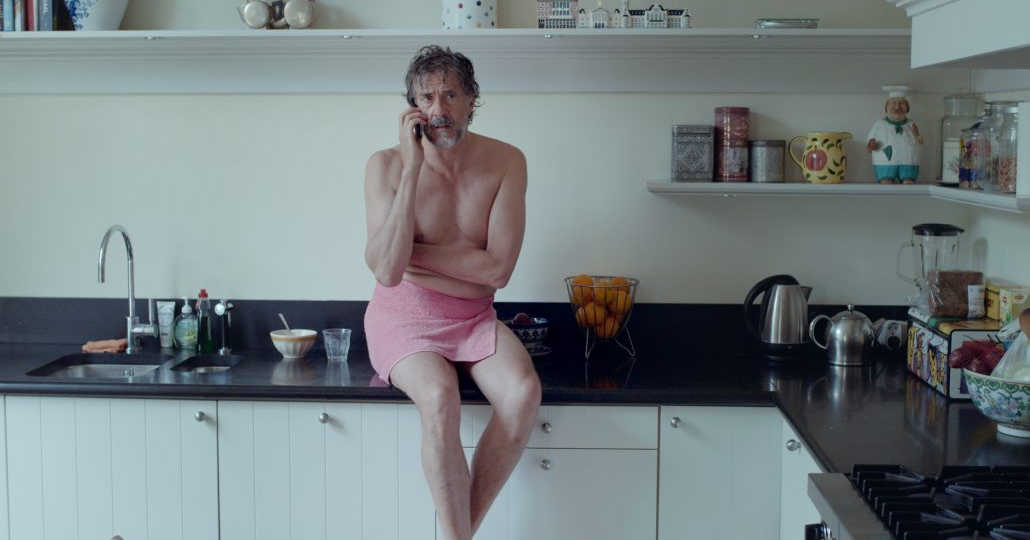 man sitting on kitchen counter wearing towel talking on phone.