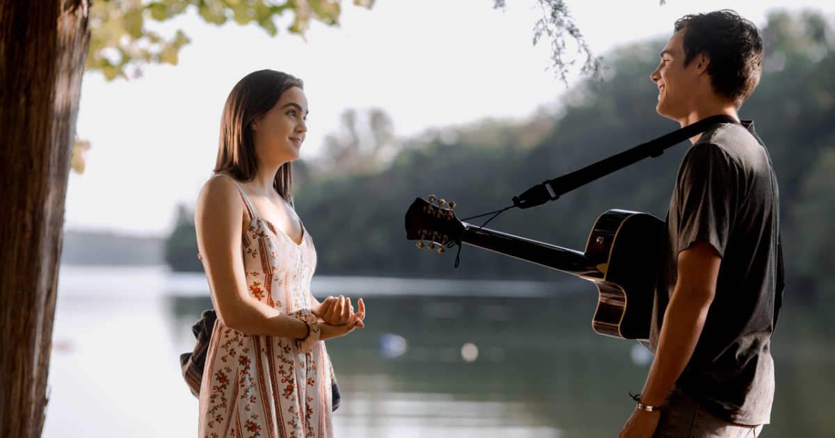 teen girl talking with teen boy with guitar by lake.