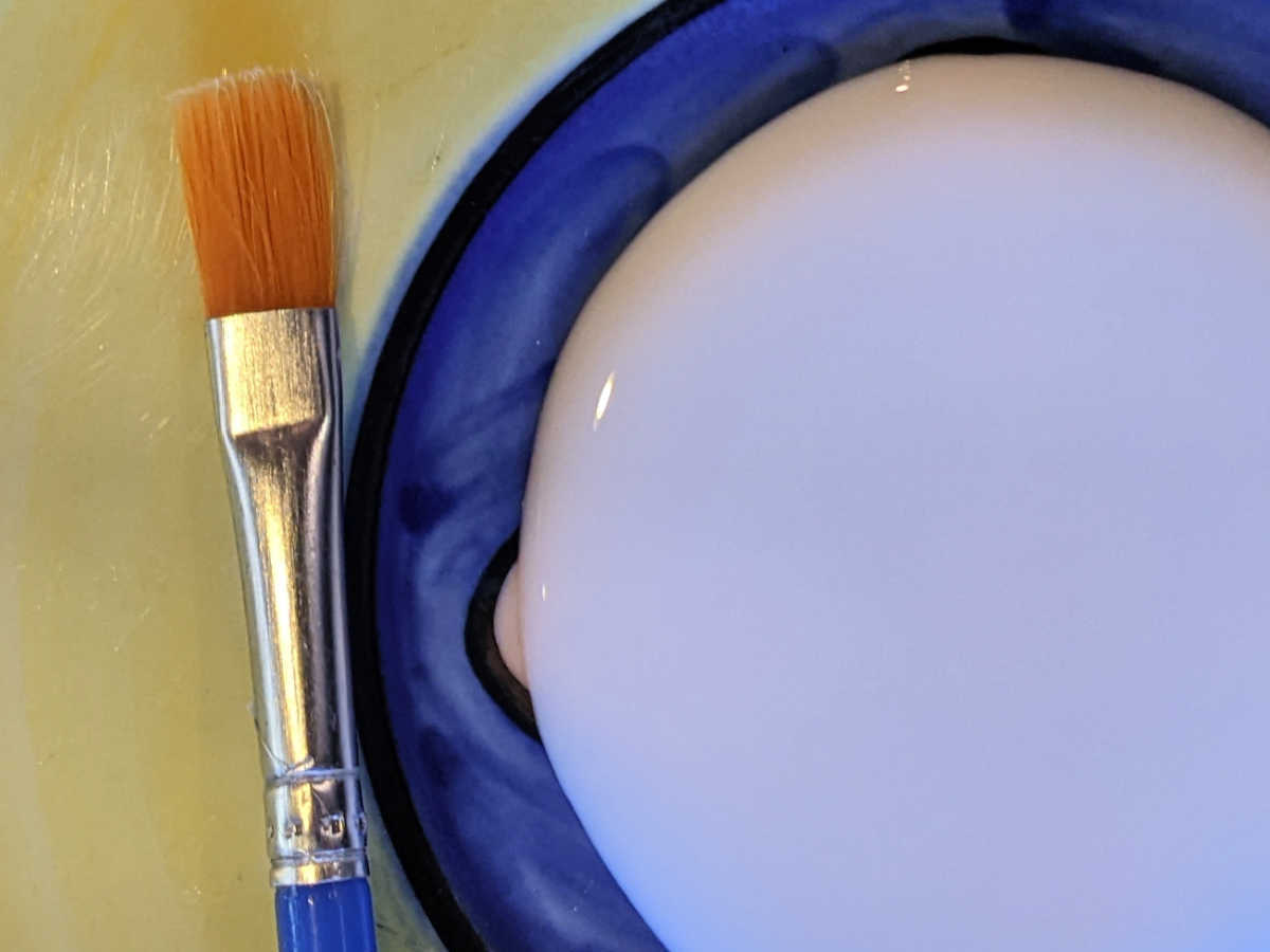 paintbrush next to glue on a plate