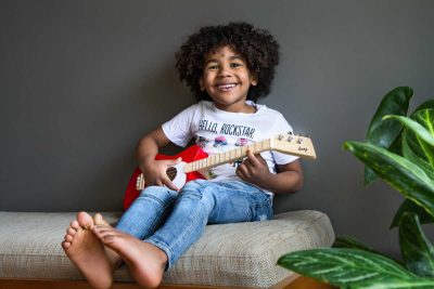 child playing red loog mini acoustic guitar