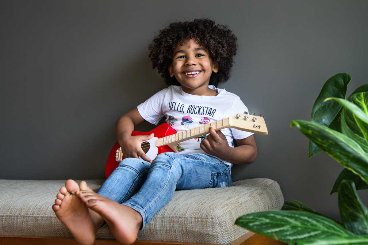child playing red loog mini acoustic guitar